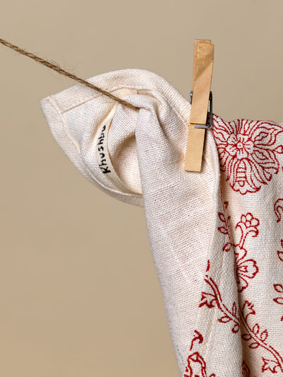 A folded corner of a red floral tea towel clipped to a clothesline, showcasing the brand's logo. Made from eco-friendly materials and hand-stitched with care.