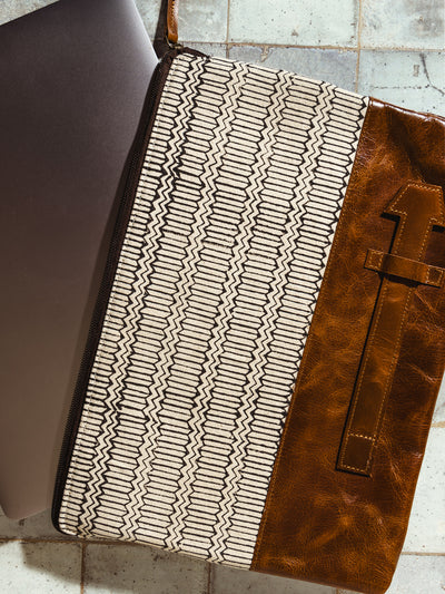 Stylish laptop sleeve featuring a geometric black and white pattern with brown leather accents, partially open to reveal a laptop inside. Perfect for modern, eco-conscious professionals.