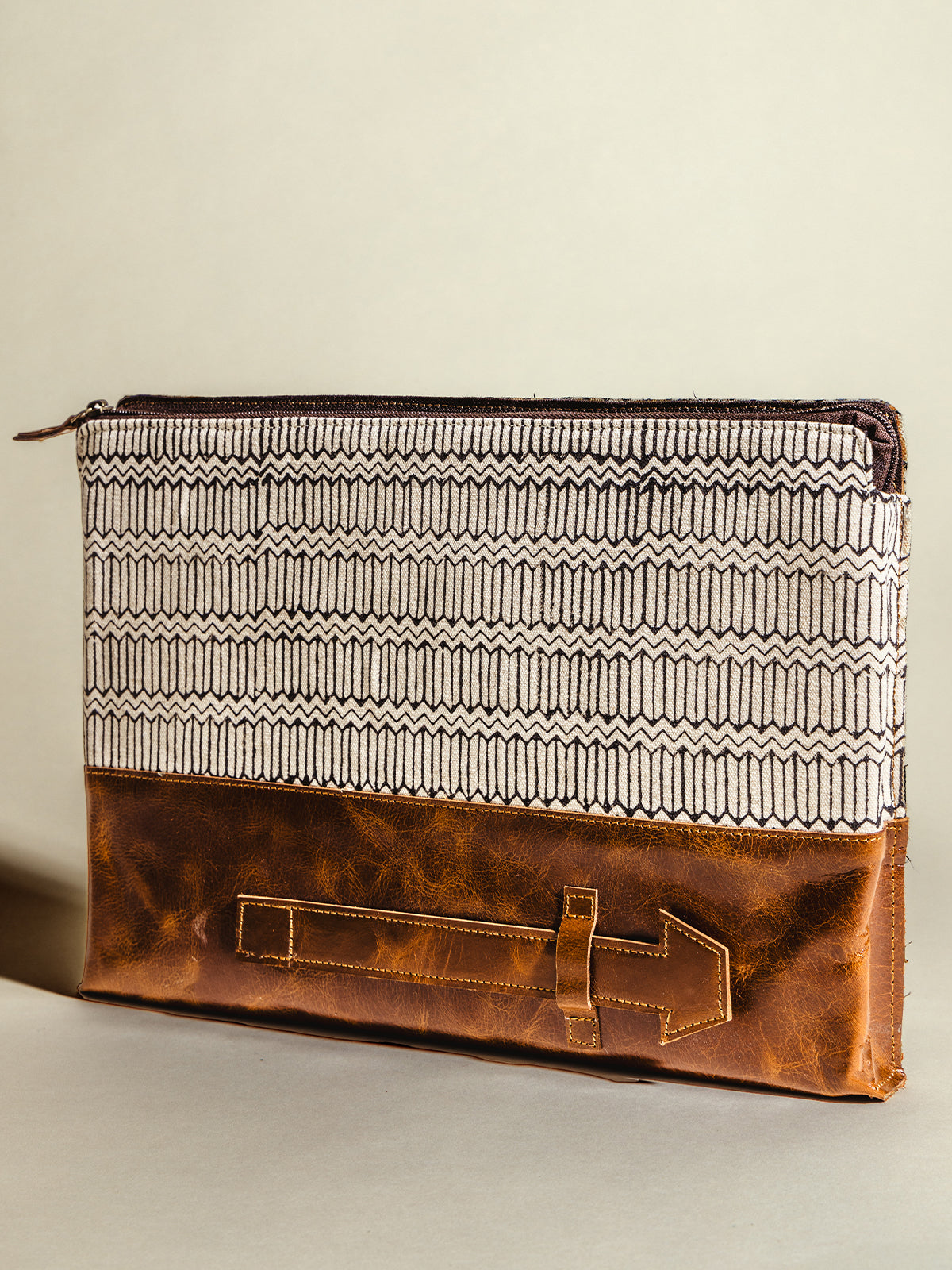 Front view of an artisan-made laptop sleeve with a black and white geometric fabric and brown leather bottom, featuring a stitched arrow design. A chic and functional accessory for work or travel.