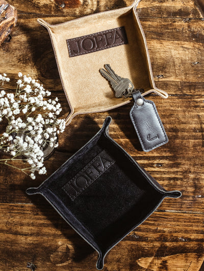 Two small leather valet tray on wooden table with keys and leather key chain.