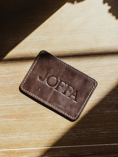 Dark brown minimalistic wallet with large logo on back. Product is on a wood surface.