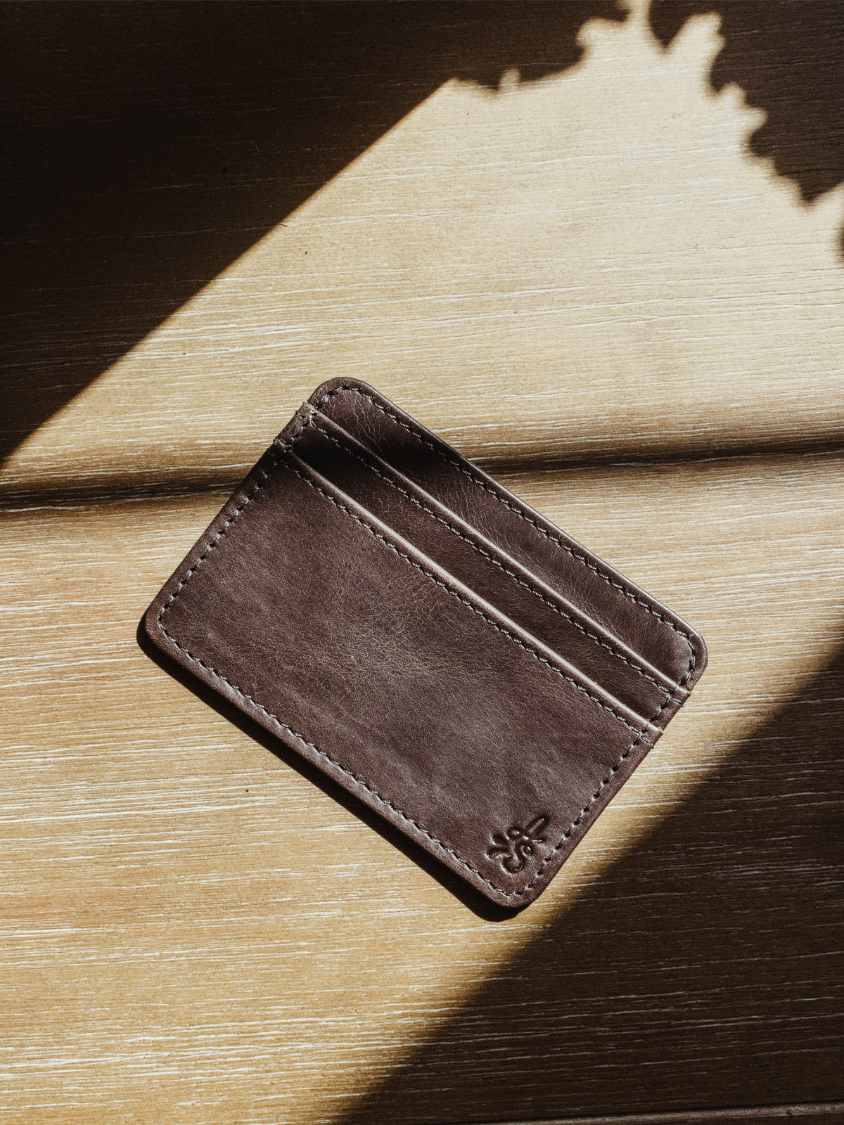 Dark brown minimalistic wallet. Product is on a wood surface.