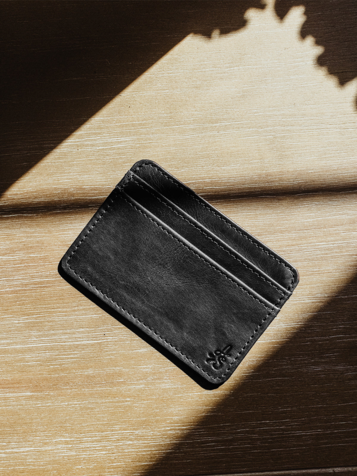 Black minimalistic wallet with large logo on back. Product is on a wood surface.