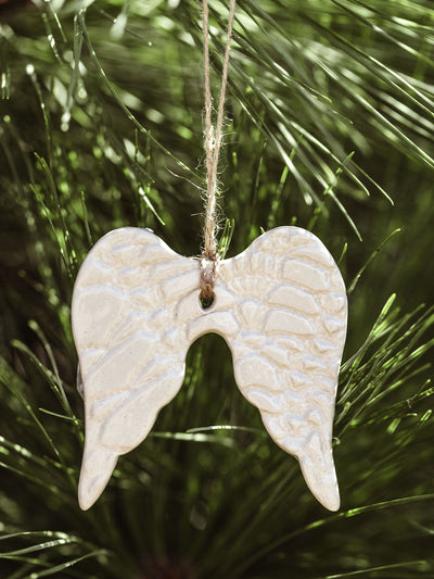 Close-up of a handcrafted ceramic angel wings ornament with intricate patterns, suspended from a natural twine on a pine tree.