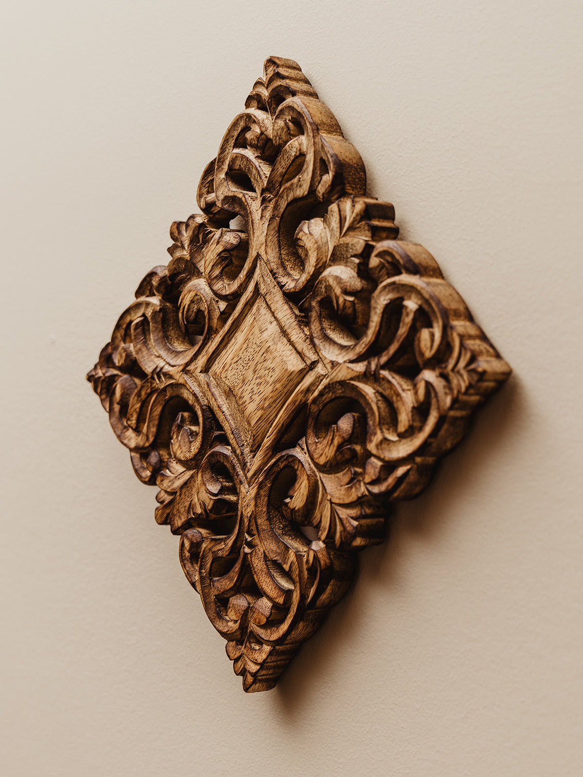 Natural ornate wood trivet hand carved and hanging on white wall as decor.