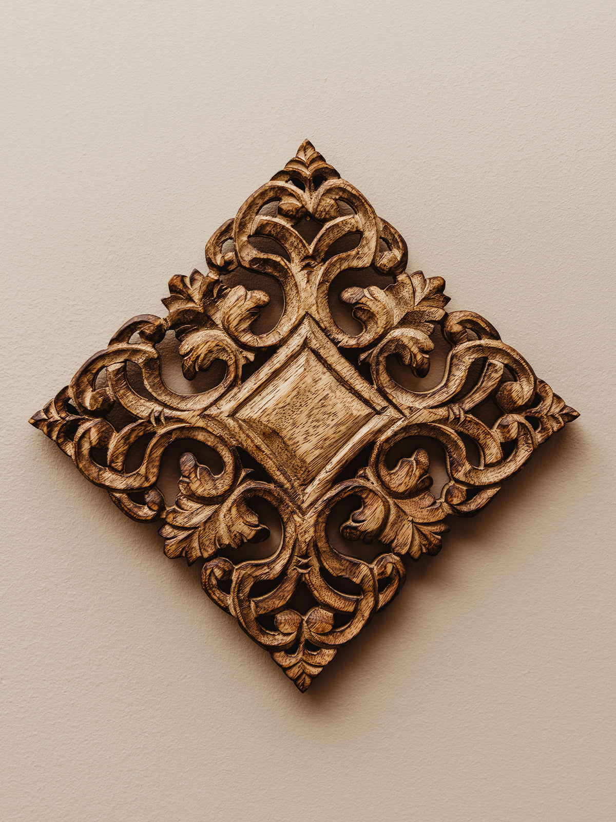 Natural ornate wood trivet hand carved and hanging on white wall as decor.