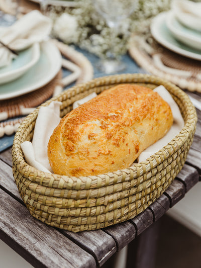 Bread warmer set on outdoor wooden with bread placed inside and surrounded by napkins on dining table. 