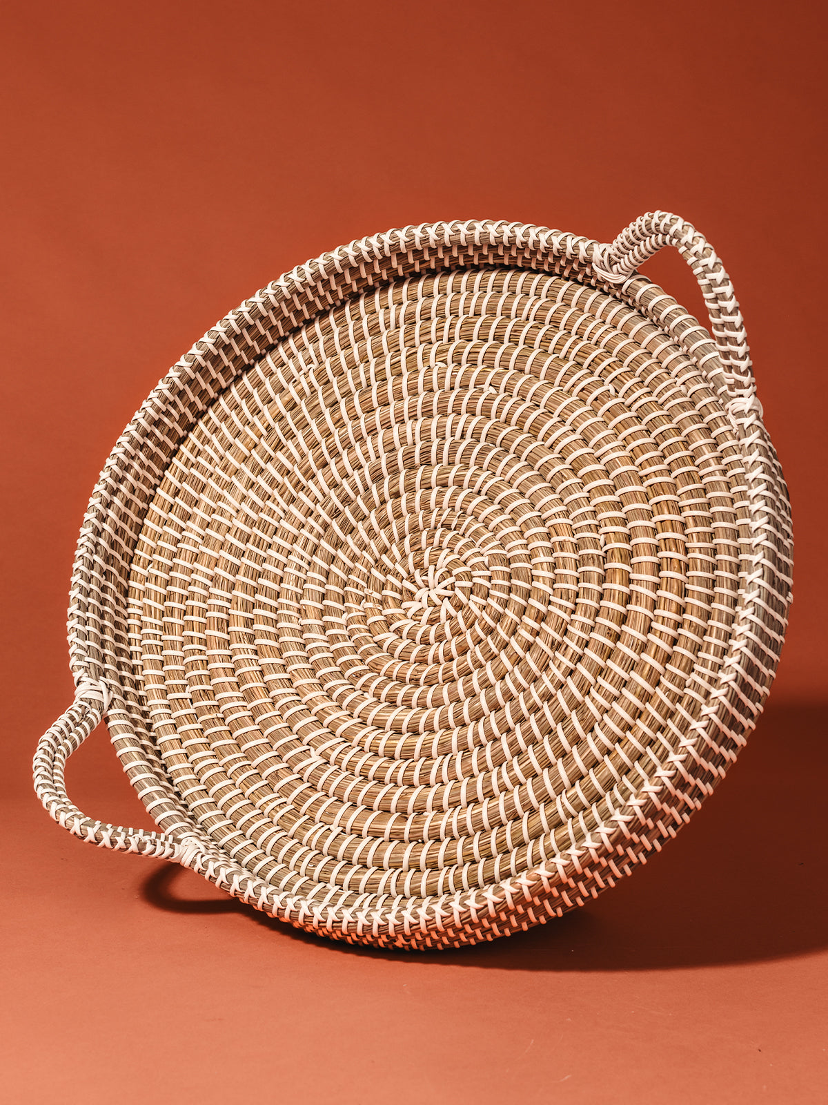 Woven Kaisa Tray on rust orange studio background.