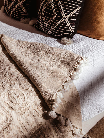 Closeup of Cream Cutwork throw blanket on cream styled bed in bedroom setting. 