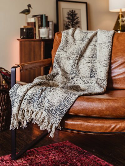 Dusk to Dawn Throw blanket on rustic red-brown leather chair in living room area.