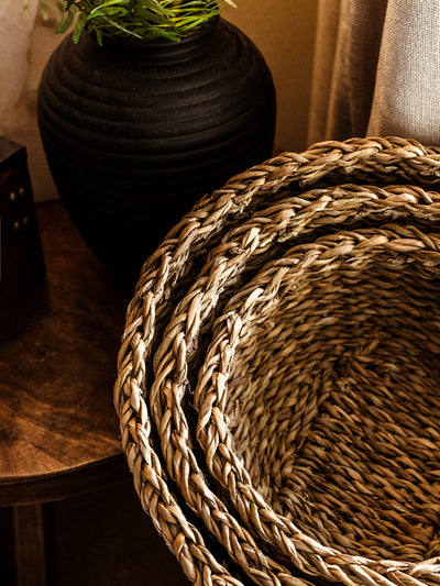 Seagrass basket set of three stacked inside one another on table with black ceramic vase.