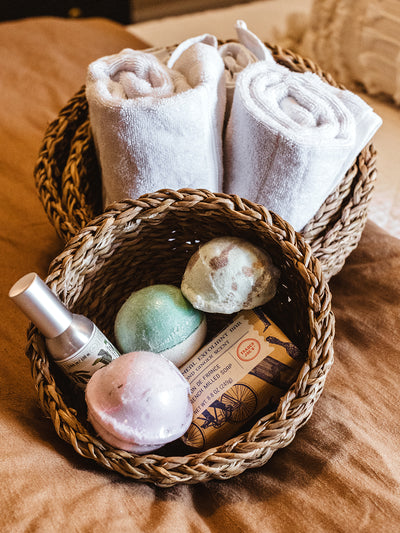 Seagrass basket set on bedding with miscellaneous items in small basket and hand towels in medium basket. 