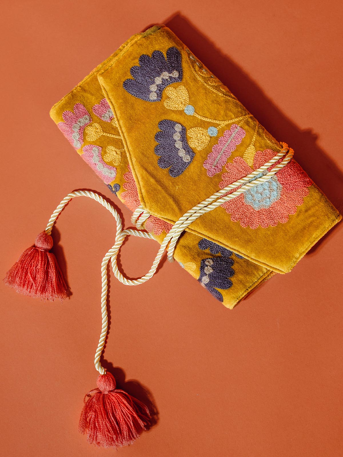 Velvet jewelry organizer with floral patter and tassel ties undone on tuscan red background.