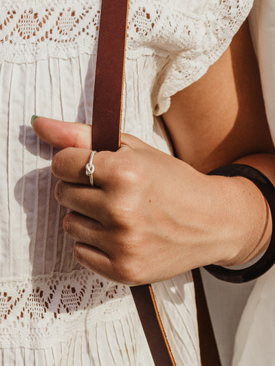 White female hand holding leather strap with silver knotted ring on finger. 