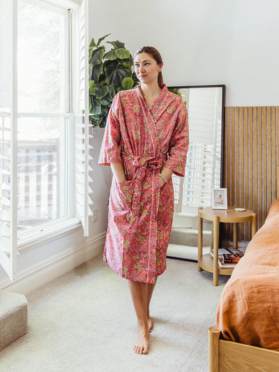 Woman standing indoors wearing a bright pink floral print robe, showcasing a vibrant, handcrafted design, available at Joffa.com as part of the sustainable loungewear collection.