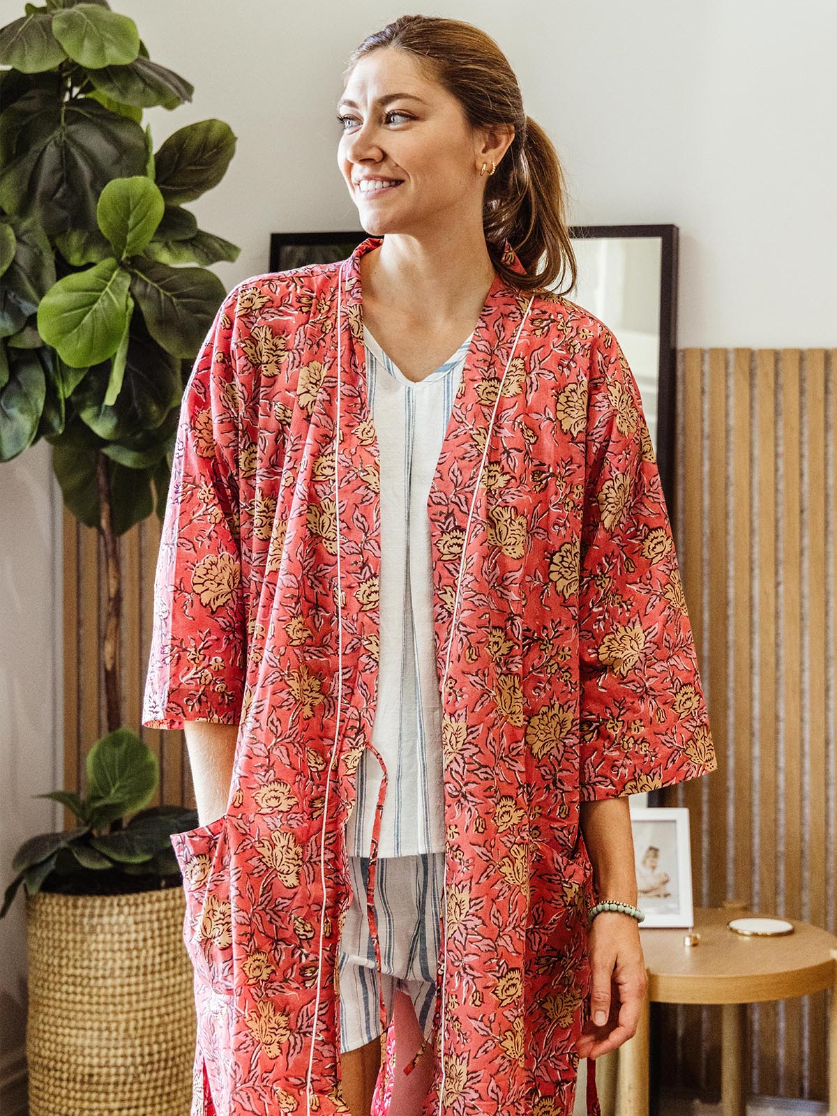 Woman smiling while wearing a bright pink floral print robe over casual loungewear, highlighting the lightweight, comfortable design, part of Joffa.com's ethically handcrafted loungewear collection.