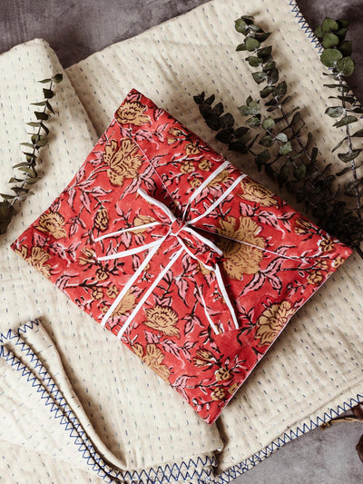 Beautifully wrapped robe featuring a red floral design, tied with a white ribbon. Displayed on a soft cream and blue quilt with eucalyptus sprigs for a touch of nature. Ethically made and perfect for gift giving.