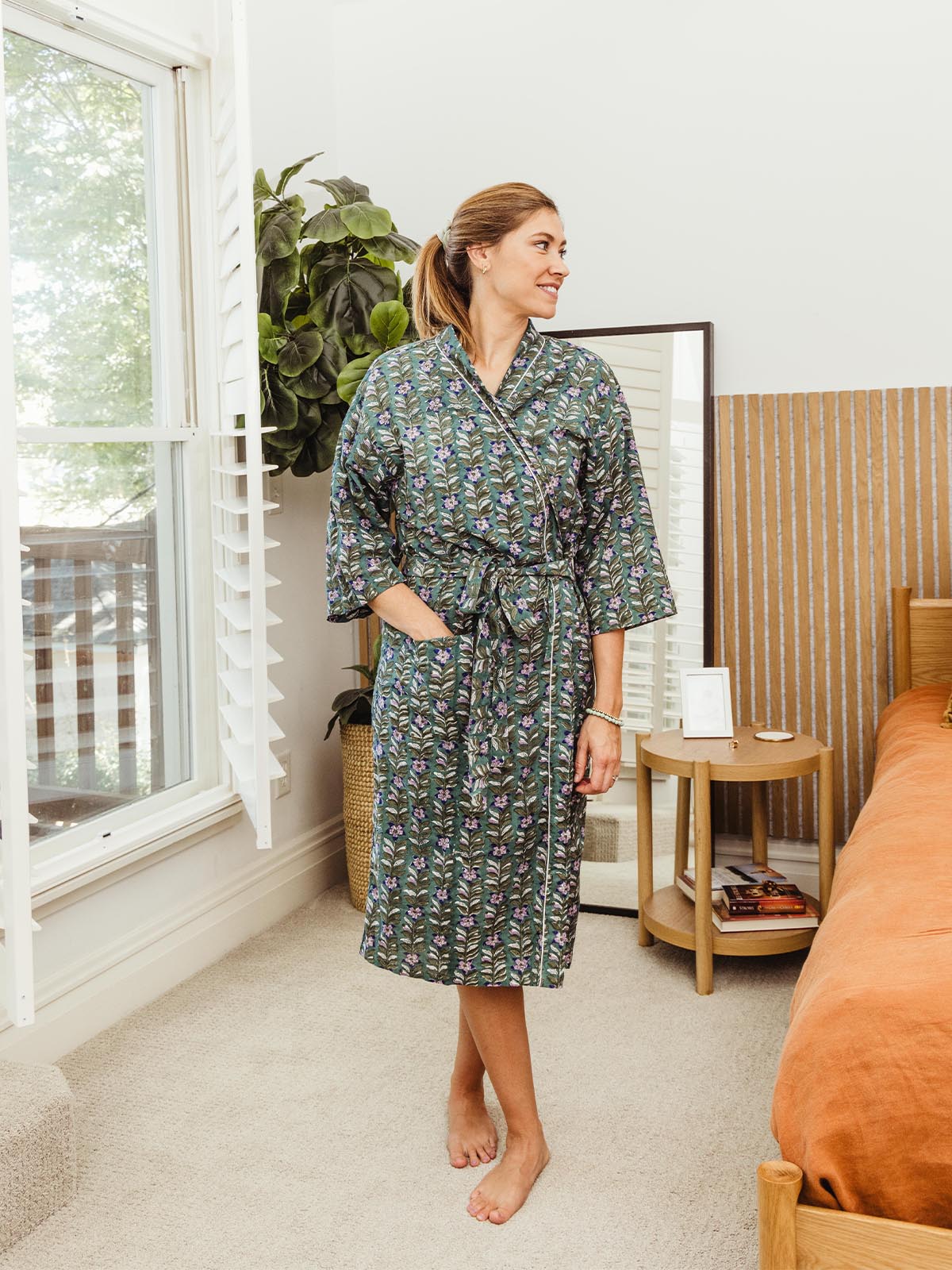 Woman standing by the window wearing a dark floral print robe, with a comfortable and relaxed fit, part of Joffa.com's ethically crafted loungewear collection.