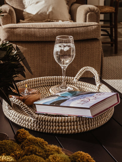 Kaisa tray with book, wine glass, and candle placed within. Tray is placed on a black coffee table in a living room space. 
