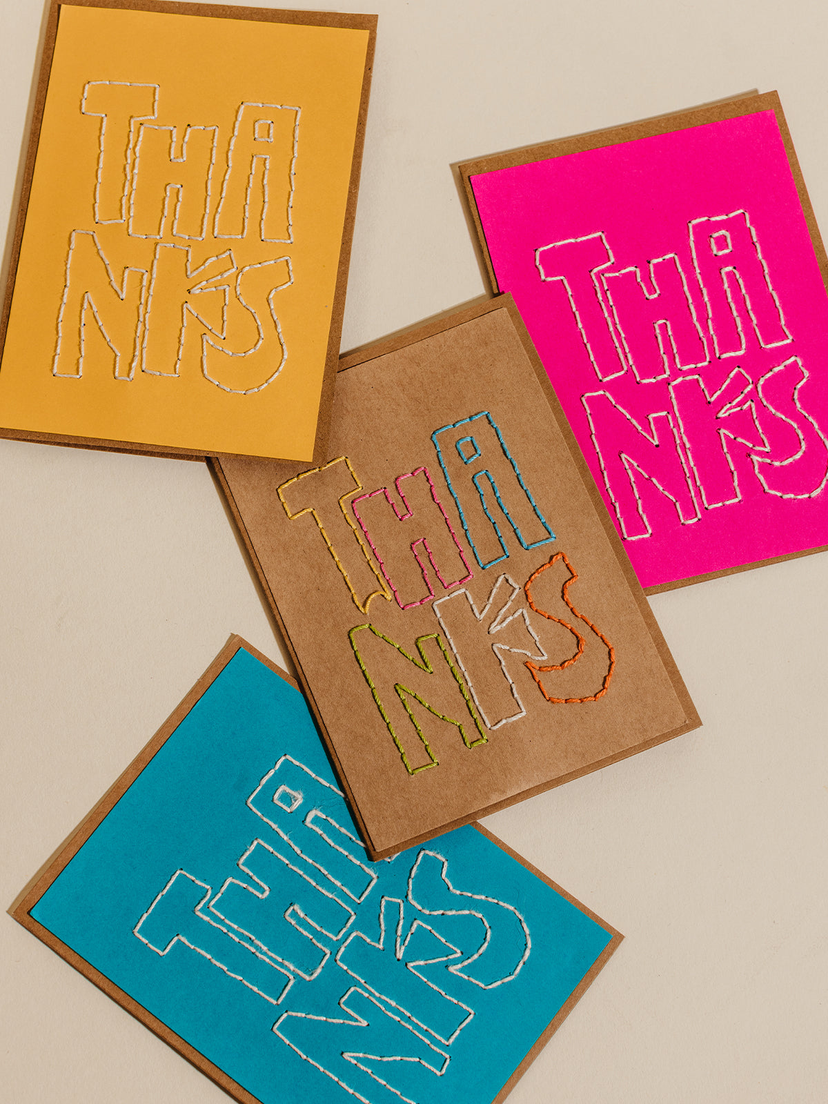 Hand-embroidered 'Thanks' cards in bold colors like yellow, pink, and blue, featuring kraft paper bases, highlighting creative and sustainable artisan stationery.