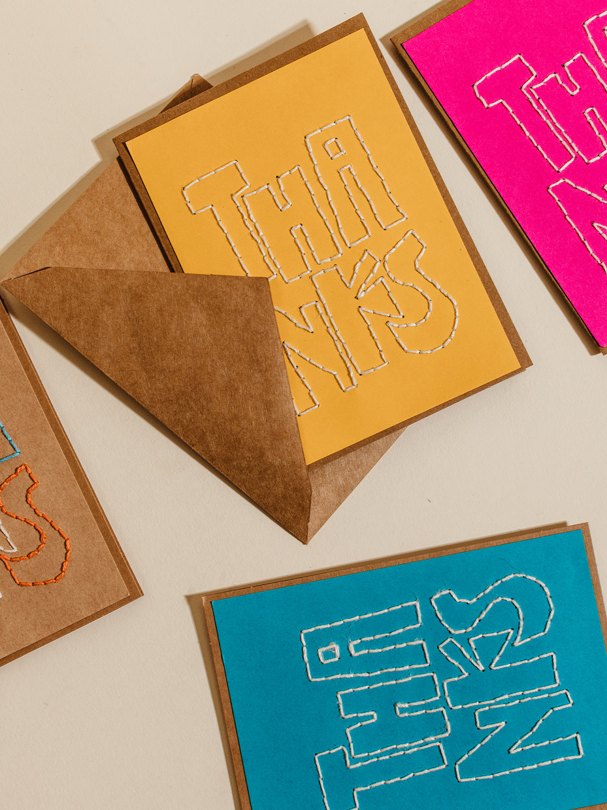 Bright and bold 'Thanks' cards with hand-stitched embroidery on colored paper, paired with brown kraft envelopes, emphasizing eco-friendly and handcrafted stationery design.