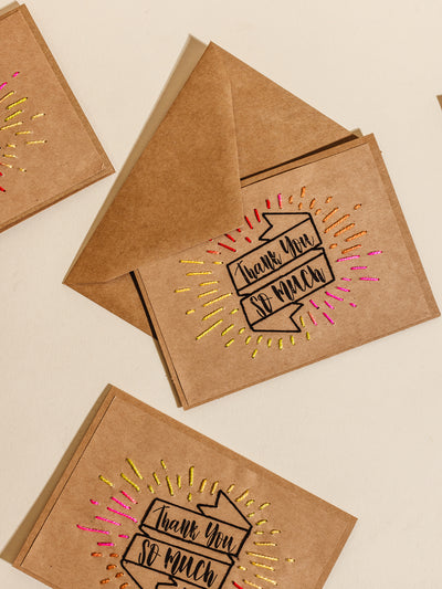 Eco-friendly 'Thank You' cards made from kraft paper with vibrant embroidered designs, paired with matching kraft envelopes, displayed on a beige surface for a minimalist and sustainable aesthetic.