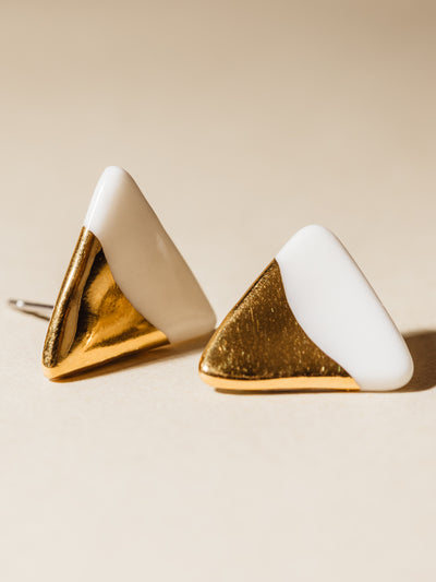 White triangle shaped clay stud earrings dipped in gold. Photographed on cream background.