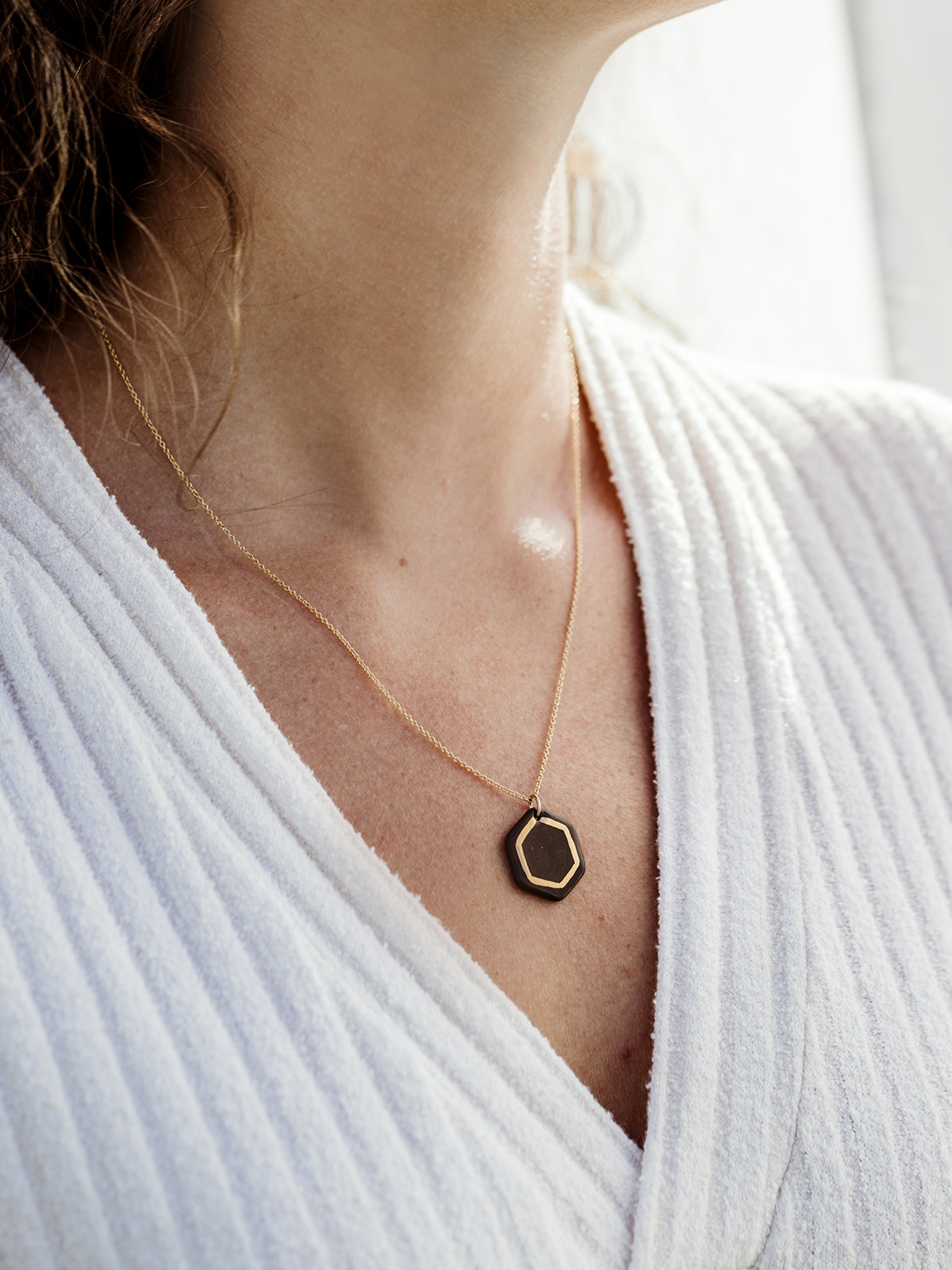 Close up image of white female model in white sweater dress on white background wearing robin hexagon necklace. 