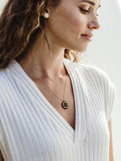 White female model in white sweater dress on white background wearing robin hexagon necklace. 