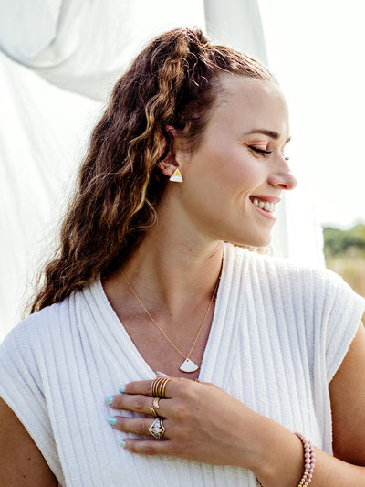 Portrait of white female in a white dress with a white background wearing various jewelry pieces and the triune studs.