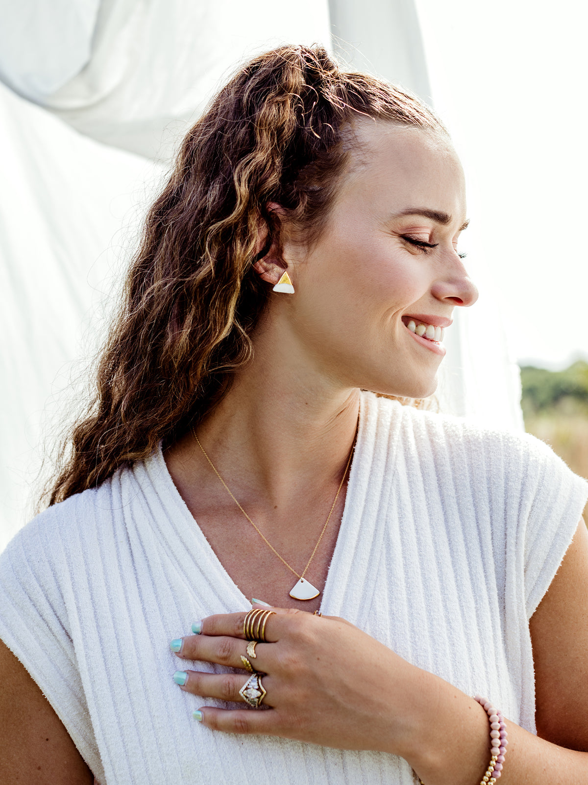 White female model wearing white dress and sojourn jewelry. Featuring the fan pendant necklace. 