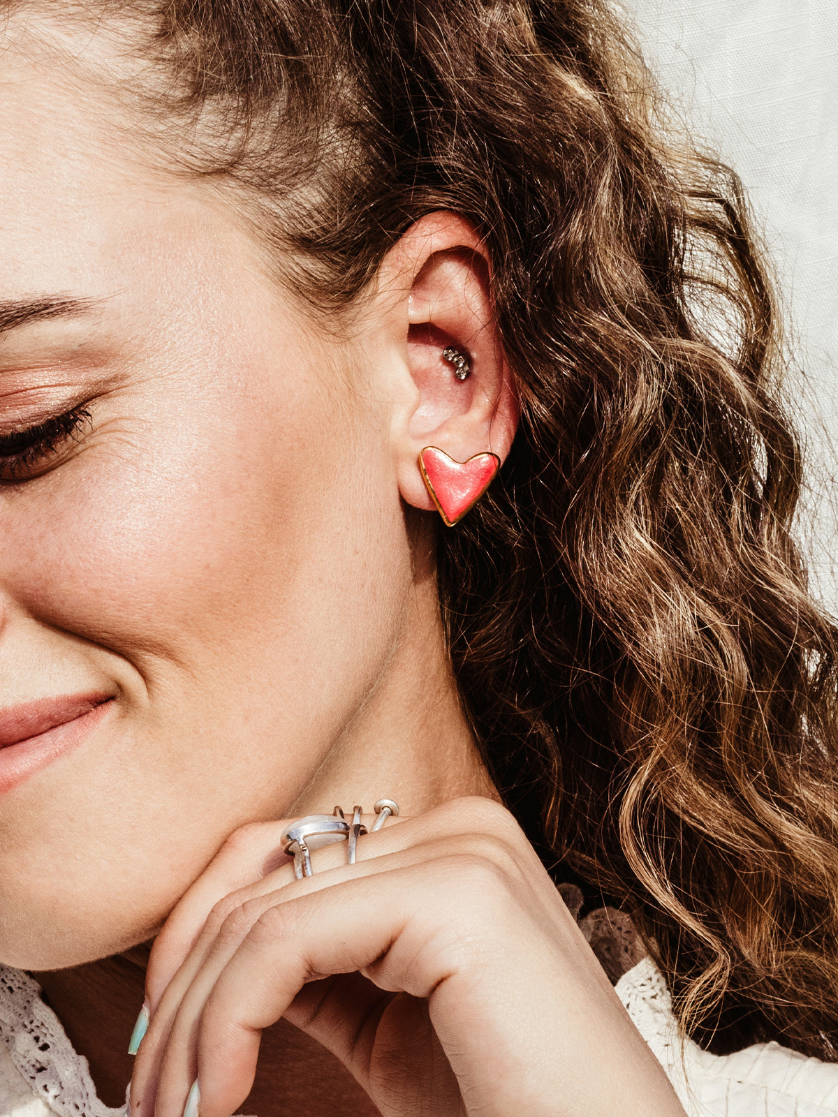 Smiling white female on white fabric background wearing red heart studs.