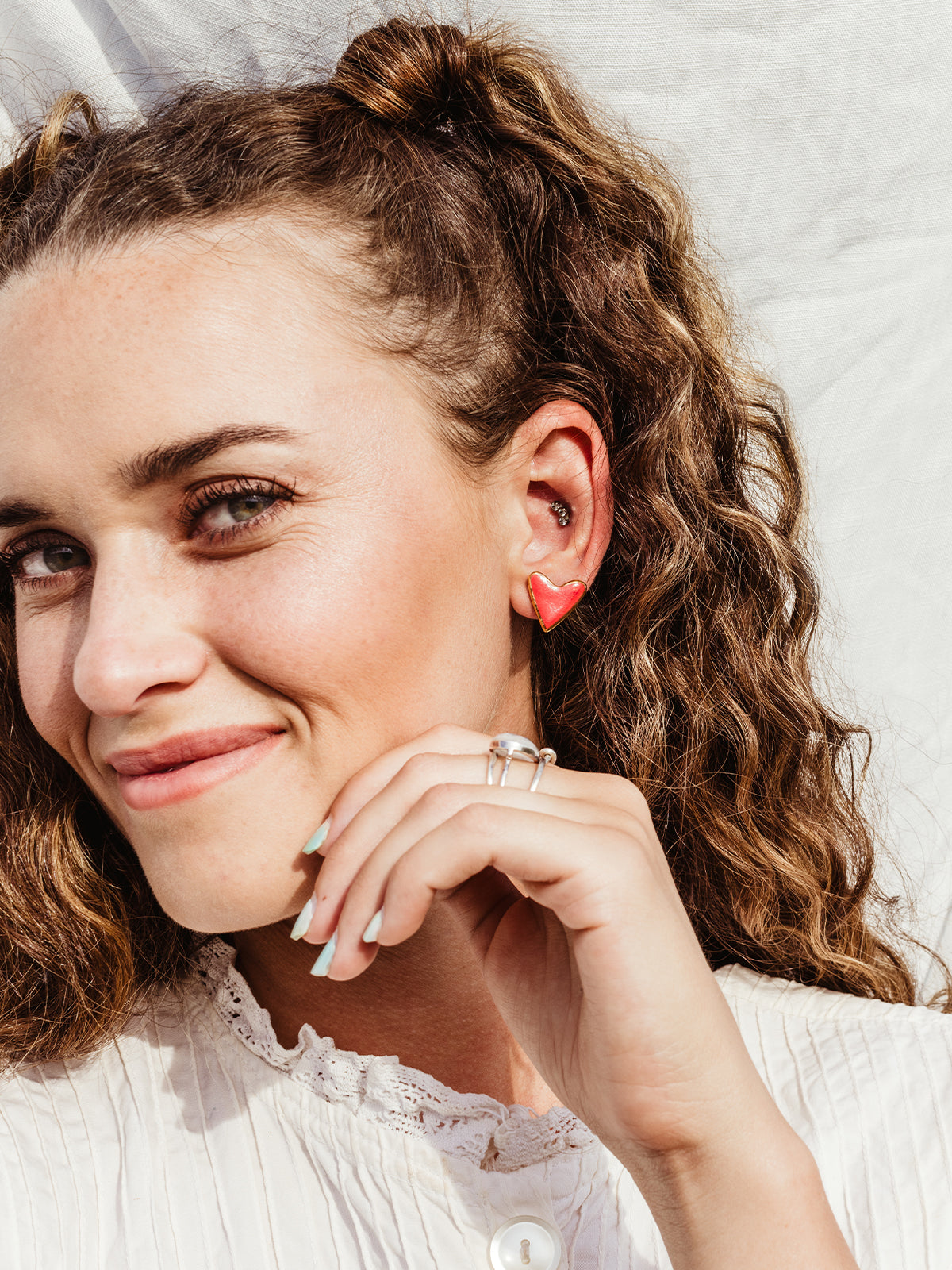 Smiling white female on white fabric background wearing red heart studs.