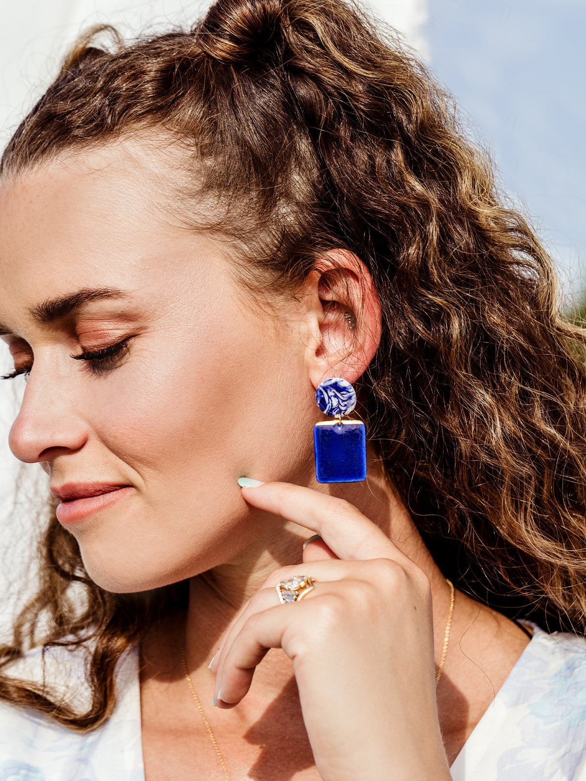 Tight image of white female wearing bright blue flourish porcelain earrings.