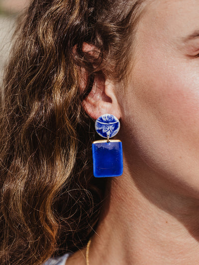 Close up image of bright blue flourish porcelain earrings with gold flake. 