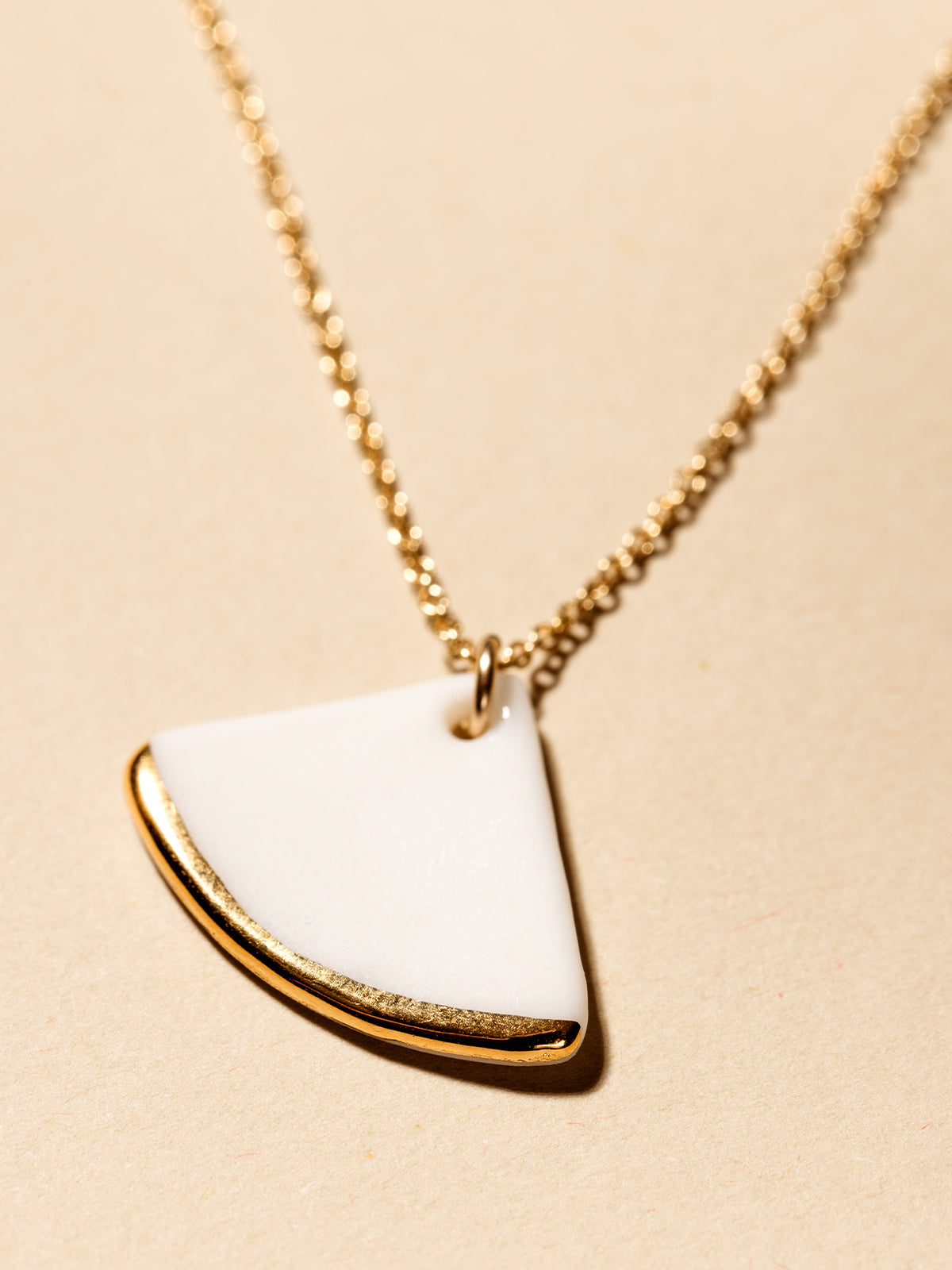 White fan necklace with close up of  gold dipped edge on cream background.