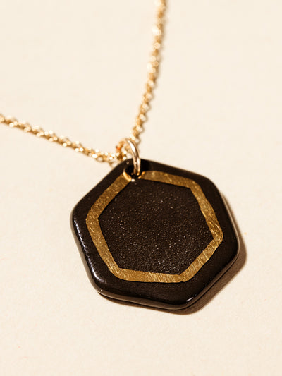 Black clay pendent necklace with gold outline inside the back pendant. photographed on a cream background. 