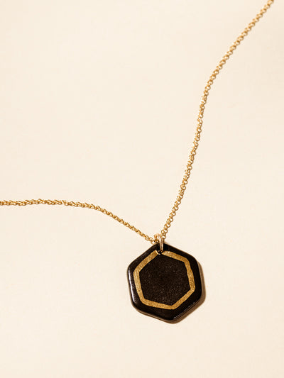 Black clay pendent necklace with gold outline inside the back pendant. photographed on a cream background. 