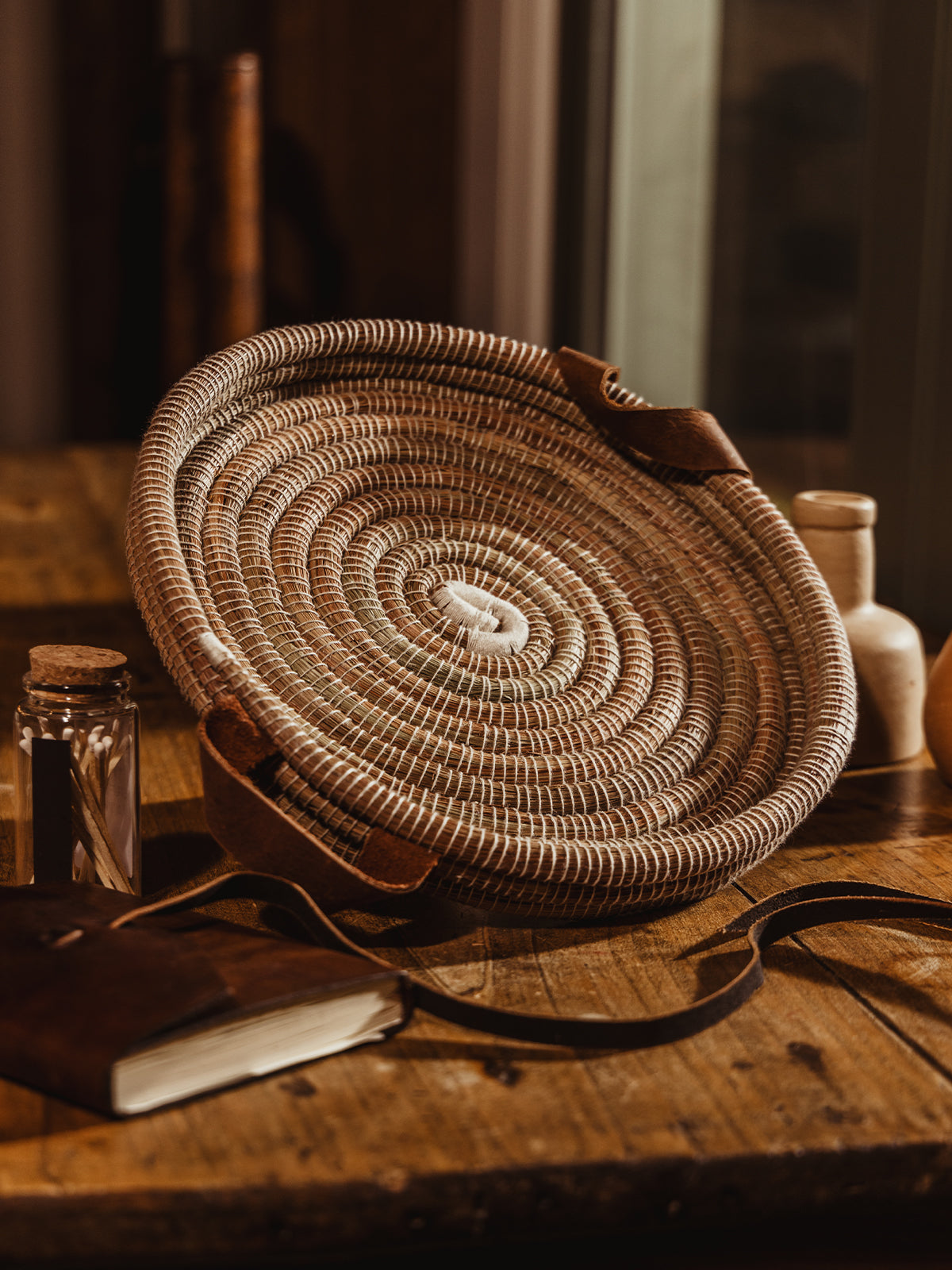 Round handwoven tray with cream center and cream threads. Tray is atop wooden table near window.