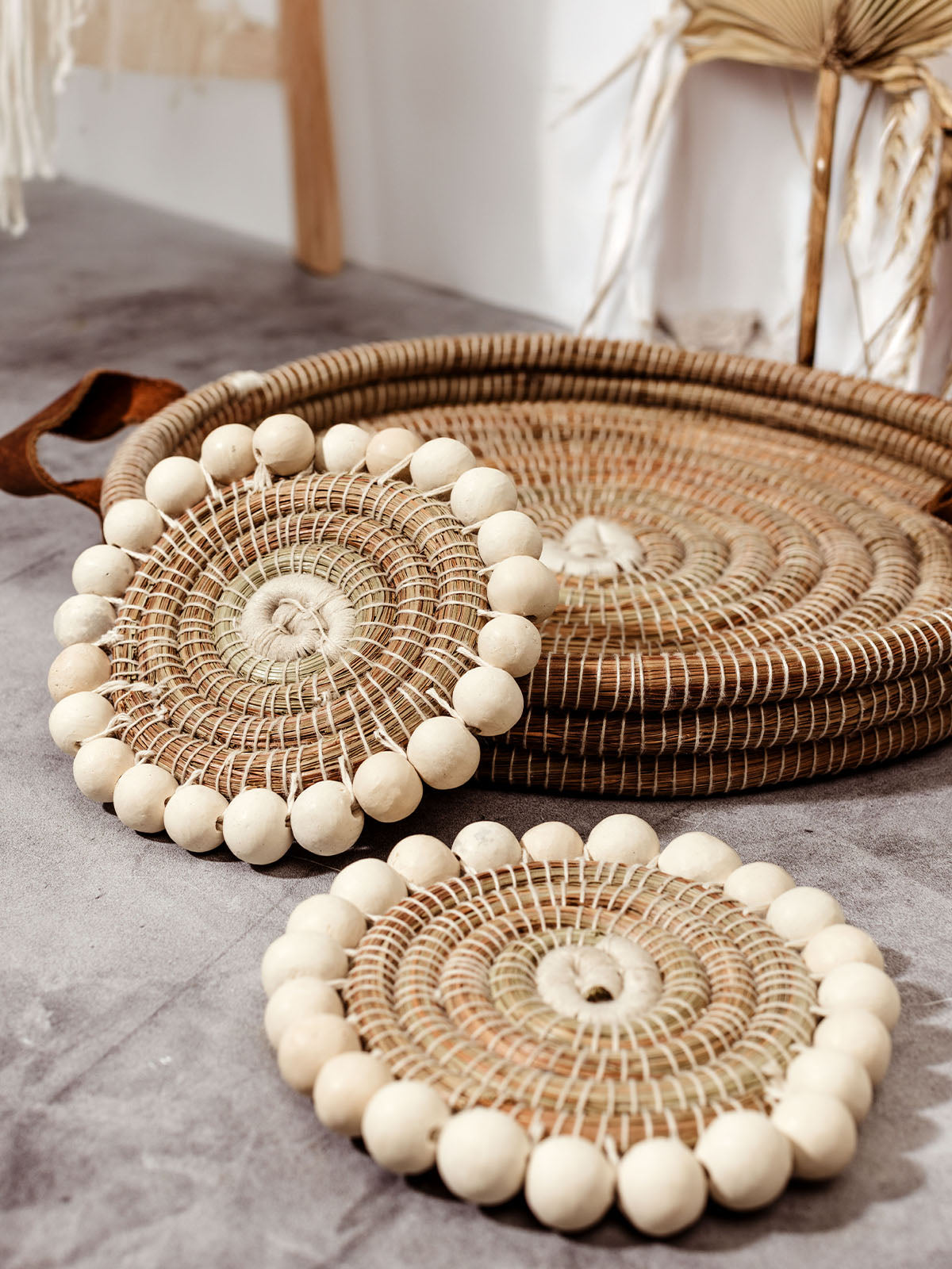 Set of two beaded coasters on concrete surface with woven tray for scale.