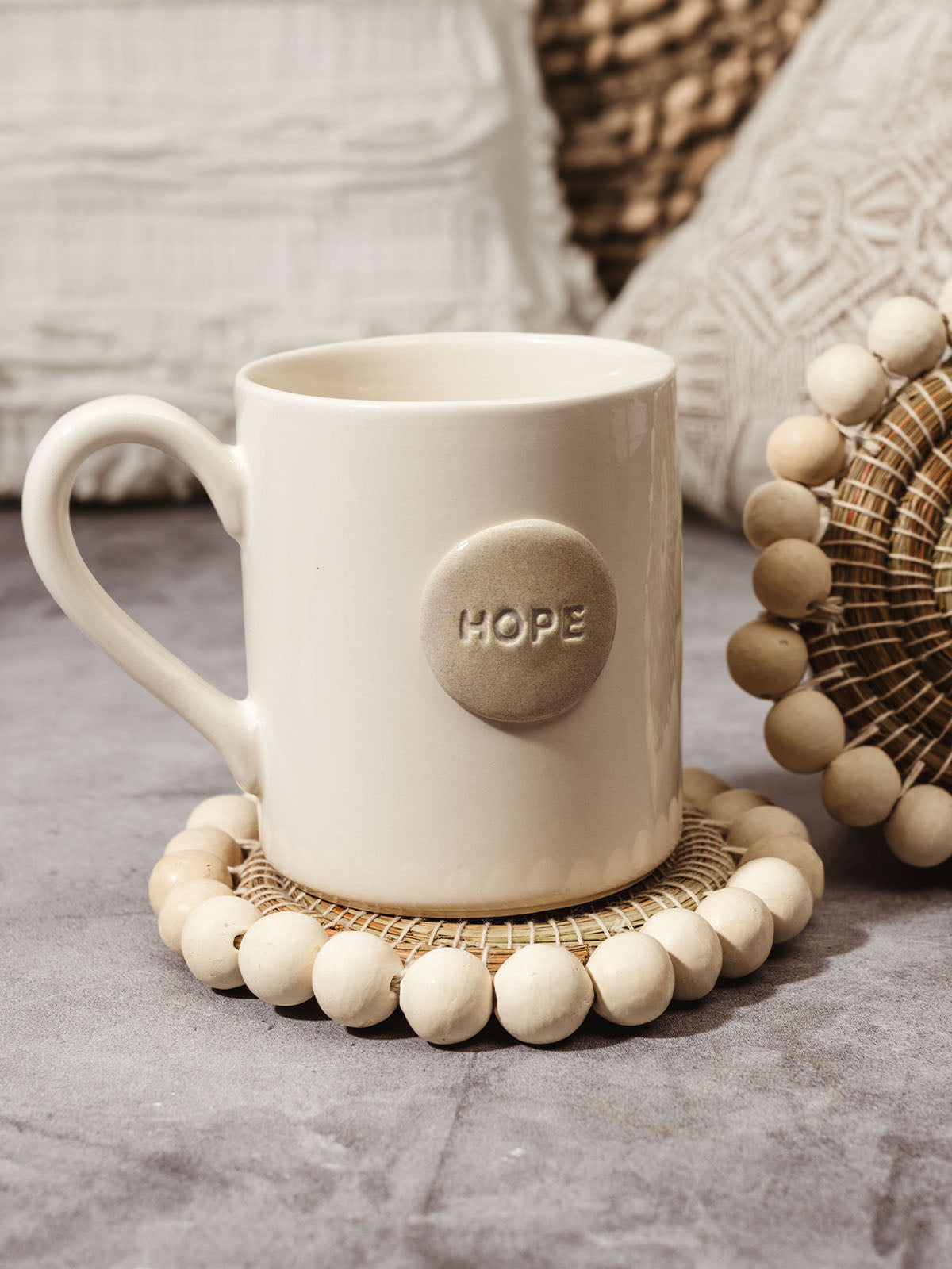 Set of two beaded coasters on concrete surface with ceramic mug that says "hope".