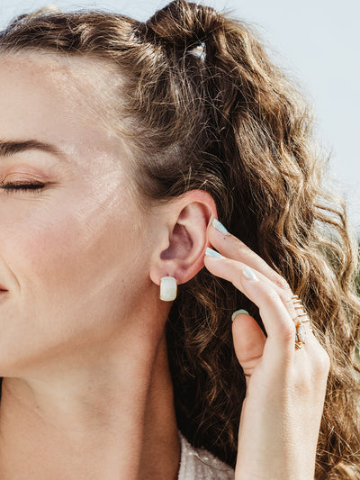 Female model wearing white ripple huggie earring.