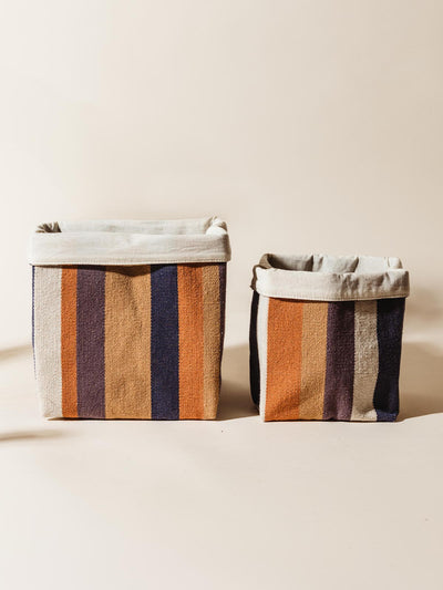 Pair of handcrafted fabric storage baskets in varying sizes, featuring vibrant orange, navy, and beige stripes, set against a neutral background.