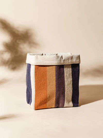 Close-up of a small handcrafted fabric storage basket with orange, navy, and beige stripes, highlighting the basket’s folded top edge.