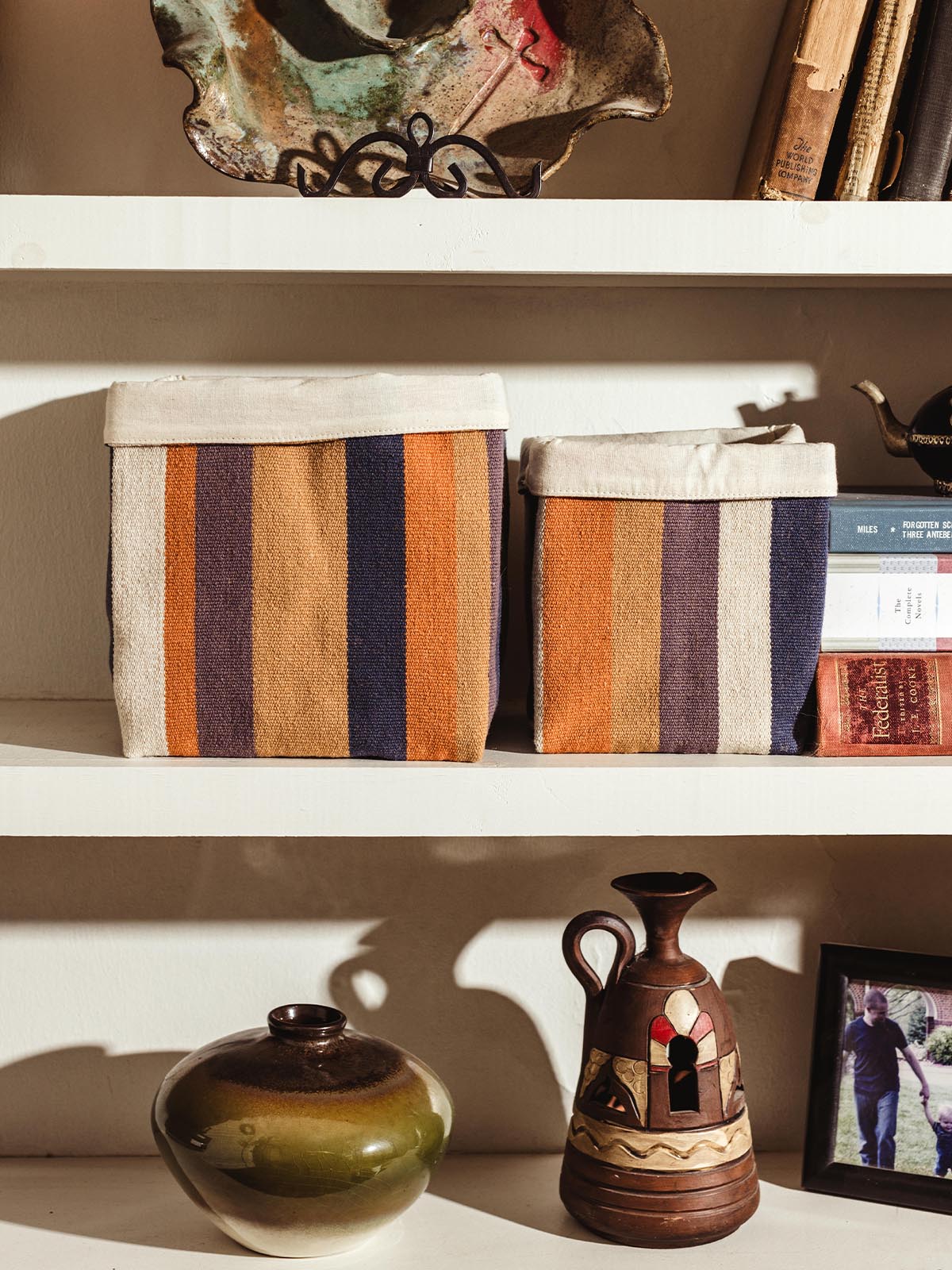 Pair of handcrafted fabric storage baskets with vibrant orange, navy, and beige stripes, neatly arranged on a shelf alongside decorative items.