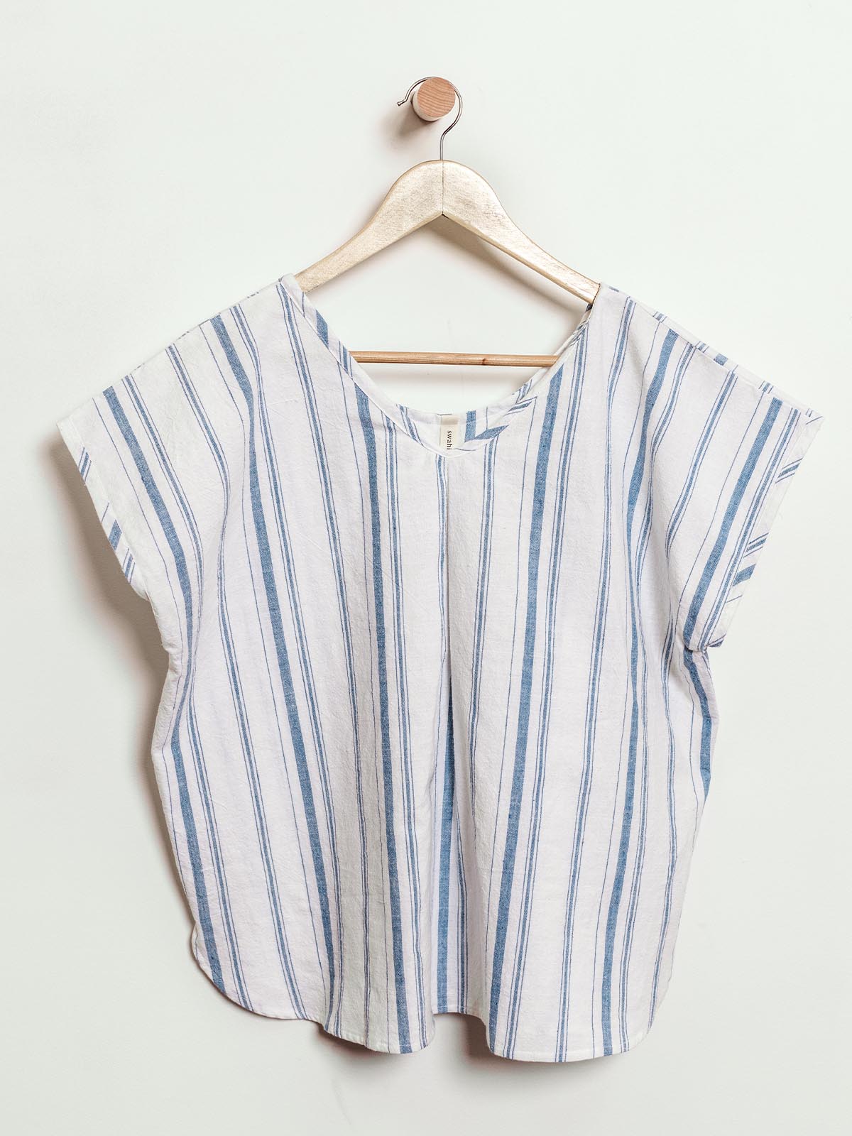 Ethically made short-sleeve top in light cream with blue vertical stripes, displayed on a wooden hanger. This relaxed-fit, v-neck shirt features a central pleat and a breezy design, perfect for casual wear and sustainable fashion lovers.