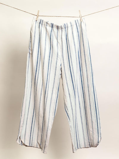 Comfortable, ethically made striped lounge pants in light cream and blue, hanging on a clothesline. These relaxed-fit, wide-leg pants feature an elastic waistband for a cozy and stylish look, perfect for lounging or casual wear.