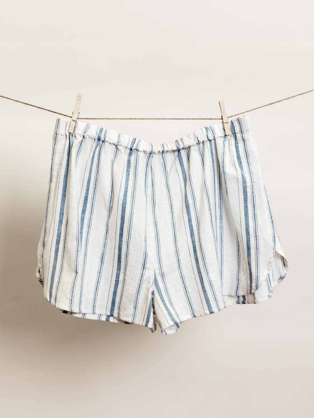 Ethically made lounge shorts with light cream fabric and blue vertical stripes, featuring an elastic waistband and relaxed fit. These comfortable, handcrafted shorts are perfect for lounging or casual wear, supporting sustainable fashion.