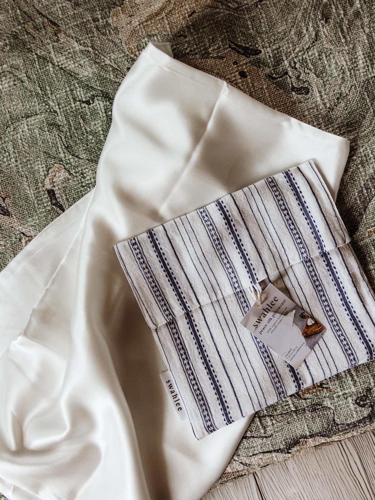 Folded white silk pillowcase with a striped fabric bag, representing a premium and eco-friendly bedding accessory.