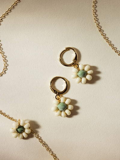 "Matching floral earrings and necklace featuring white bead petals with soft green centers on gold hardware, displayed on a light cream background, highlighting handcrafted artisan jewelry with a delicate and sustainable design.